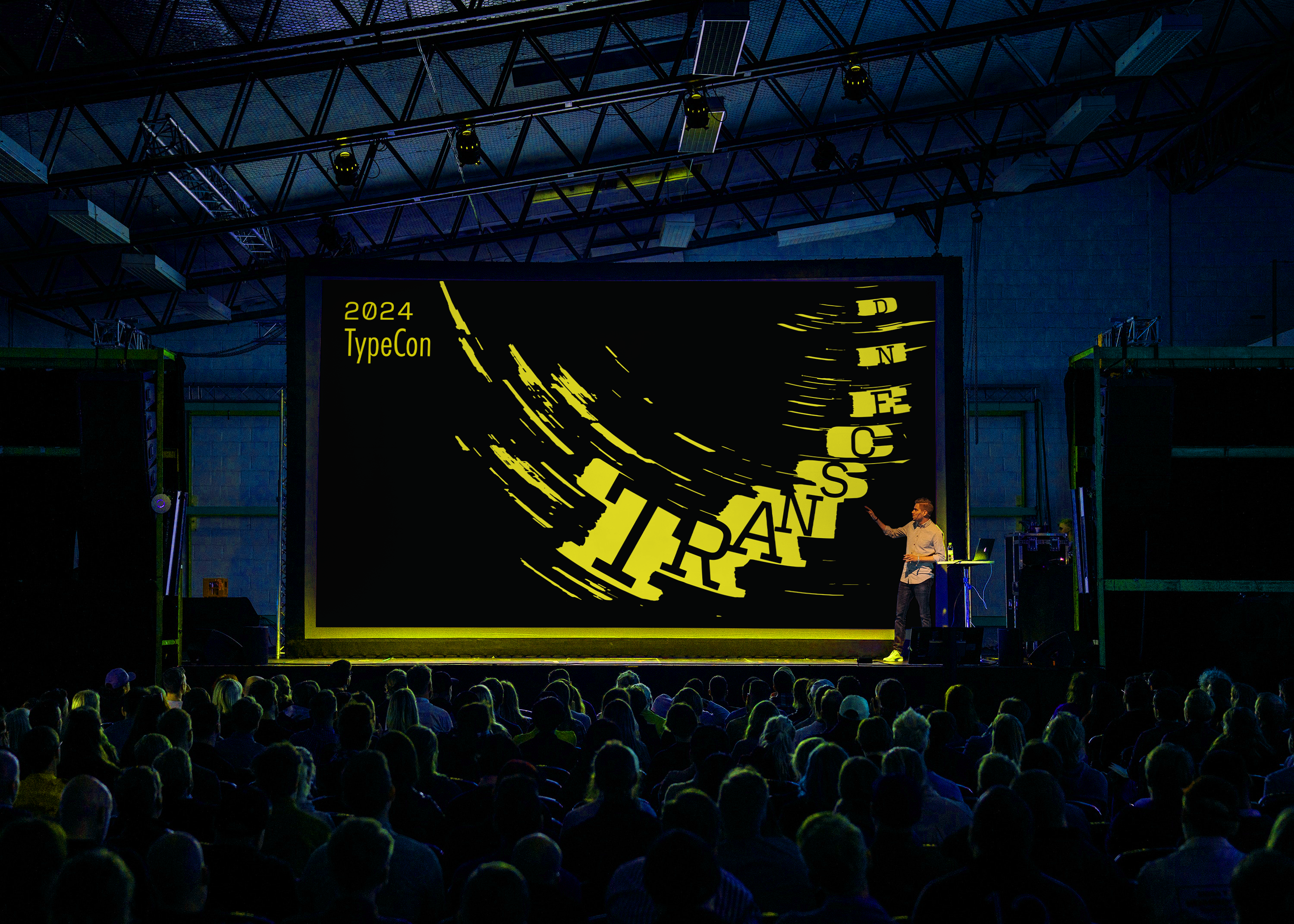 A person introducing the transcend speaker on a big screen in front of a crowd.